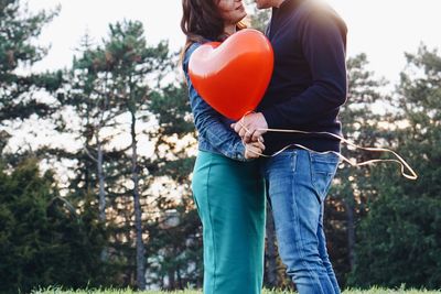 Midsection of man holding woman standing against trees