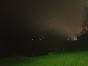 Defocused image of illuminated field against sky at night