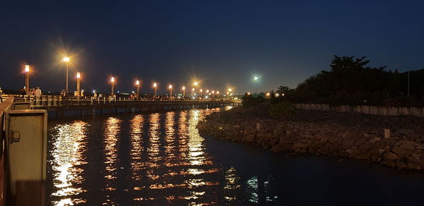 Illuminated street lights by river against sky at night