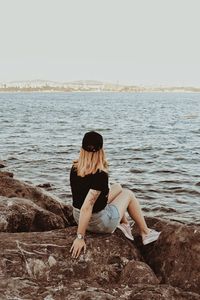 Woman sitting on rock looking at sea against clear sky