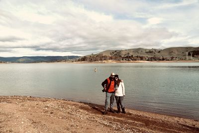Portrait of couple standing at lakeshore against sky