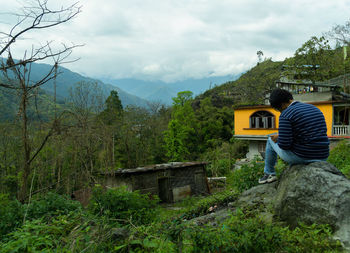 Rear view of teenage girl sitting on mountain against sky