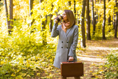 Woman holding umbrella while standing by tree in forest