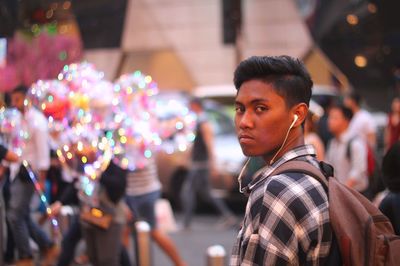 Portrait of young man with backpack standing on street in city