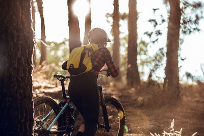 Back view of human with backpack riding on bicycle on path between trees on hill in forest person