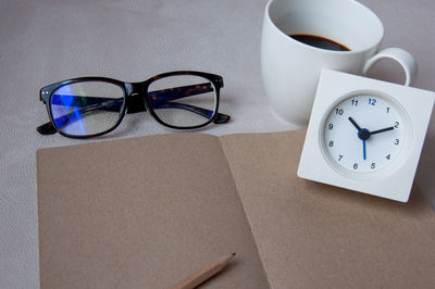 High angle view of brown paper with clock and cup by eyeglasses