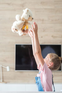 Side view of girl playing with teddy bear at home