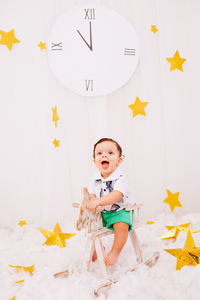 Cute boy sitting against clock on wall