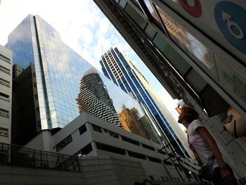 Low angle view of woman standing by skyscraper against sky