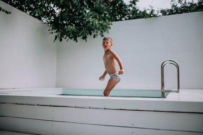 Full length of shirtless man standing by swimming pool