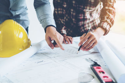 Midsection of engineer with colleague drawing on blueprint