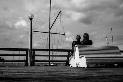 People sitting on bridge against sky