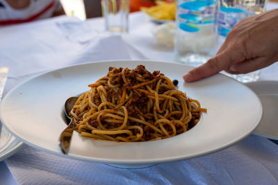 Plate full of spaghetti bolognese. finger pointing at food.