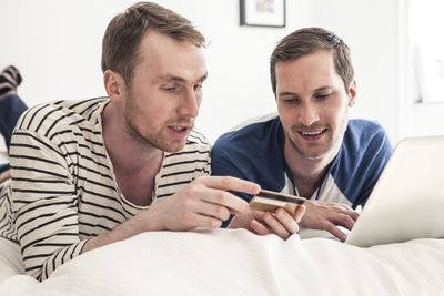 Homosexual couple shopping online on laptop together while lying in bed at home