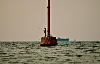 Man fishing while standing on metal structure amidst sea