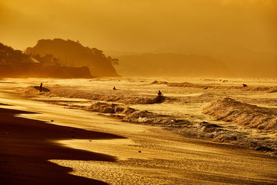 People walking at surfer beach against golden sky during sunrise