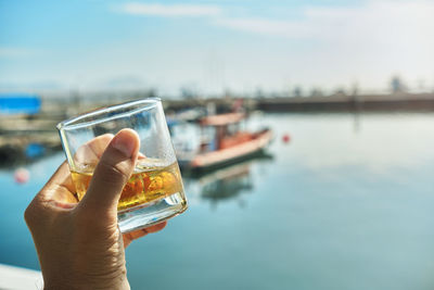 Male hand holding glass whiskey the beginning of summer at marina, summer concept.
