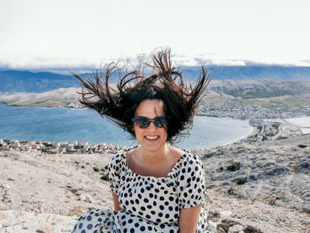 Portrait of smiling young woman on land against sea