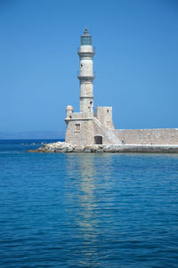 Lighthouse by sea against building against clear blue sky