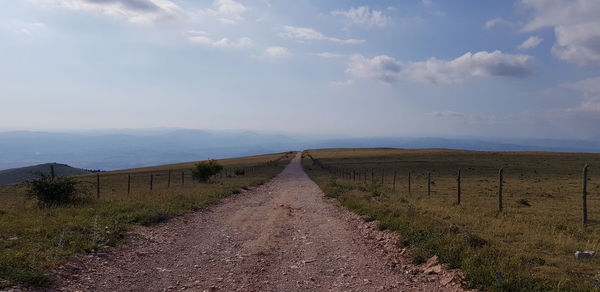 Dirt road amidst field against sky