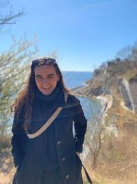 Portrait of smiling young woman standing against sky