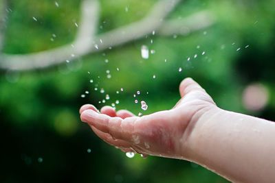 Raindrops falling on cropped hand of person