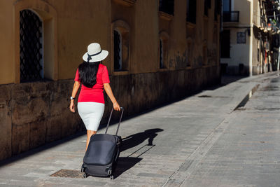 Rear view of woman walking on footpath amidst buildings in city