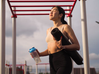 Young beautiful woman asian appearance in outdoor training  with bottle of water and sport cerpet 