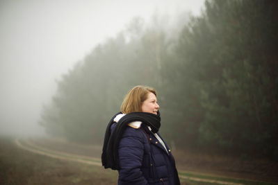 Woman standing by forest in foggy weather