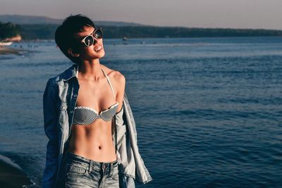 Happy young woman standing by sea