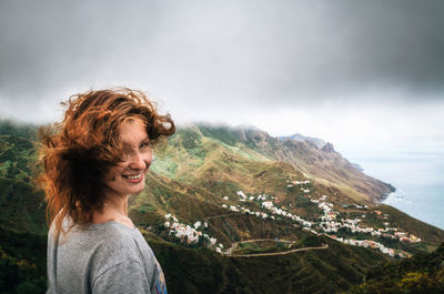 Smiling young woman by mountains against sky