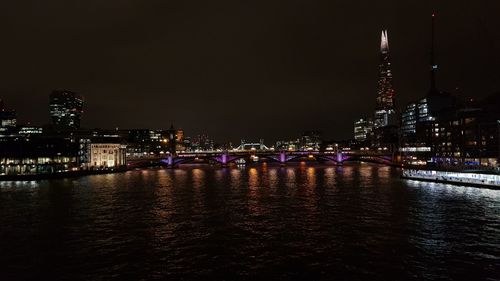 Illuminated buildings by river against sky at night