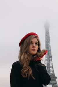 Portrait of young woman standing against clear sky and eiffel tower