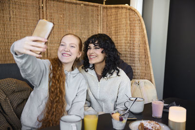 Smiling young women taking selfie in cafe