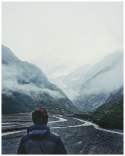 Rear view of man looking at mountains against sky