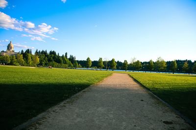 Dirt road amidst field against sky