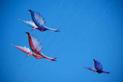 Low angle view of kites flying against clear blue sky