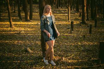 Portrait of young woman standing on tree trunk in forest