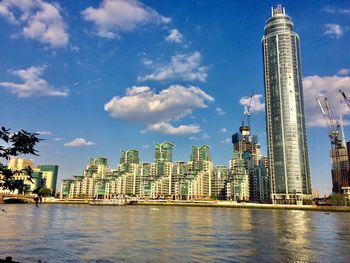 Modern buildings by river against sky in city