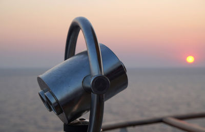 Close-up of coin-operated binoculars against sea during sunset