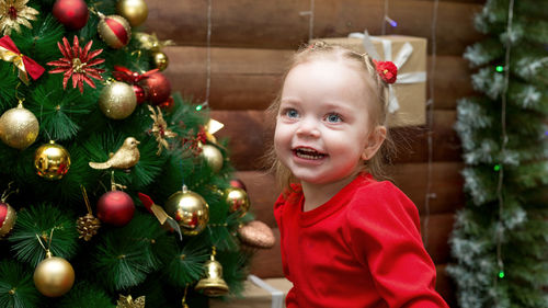 Portrait of a happy little girl in a red dress  wooden background with a decorated christmas tree.