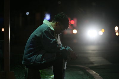 Side view of man looking at illuminated street at night