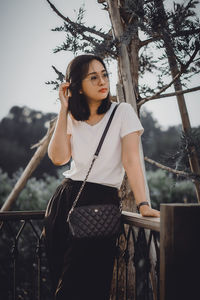 Portrait of young woman standing against trees