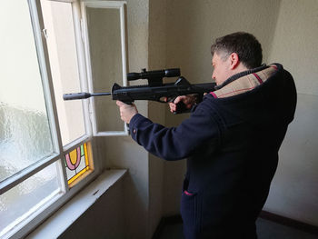 Man aiming sniper rifle through window