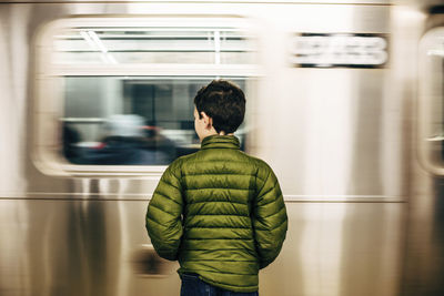 Rear view of boy wearing green jacket while standing at subway station