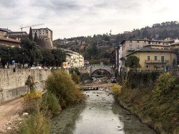 Arch bridge over river amidst buildings in city against sky