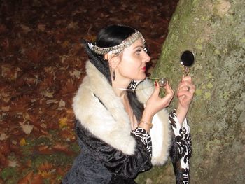 Young woman holding mirror and pendant by tree at night