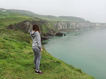 Side view of young woman standing on mountain by sea at giant causeway