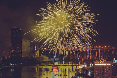 Firework display over illuminated buildings and river in city at night