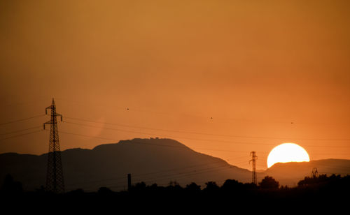 Silhouette electricity pylons against orange sky